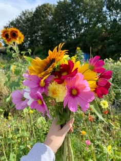 a person is holding a bouquet of flowers in their hand and there are sunflowers in the background