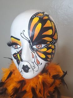 a woman's face painted with orange and black feathers on a mannequin