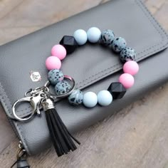 a black and pink bracelet with tassels sits on top of a gray purse