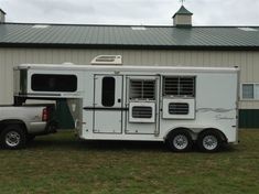 a white horse trailer parked in front of a building with a metal roof and green grass