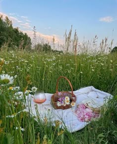 a picnic blanket in the middle of a field with flowers and wine glasses on it