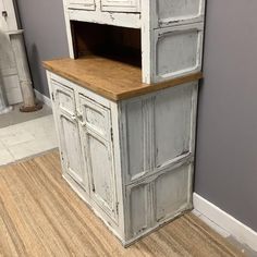 an old white cabinet with wooden top in a room next to a gray wall and hardwood floor