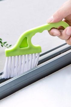 a hand holding a green brush on top of a window sill