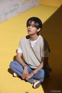 a boy sitting on the ground with his skateboard in front of him and wearing a hat