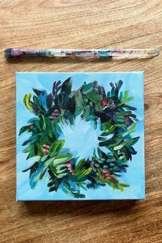 a painting of a wreath on a blue background next to a paintbrush and pencil