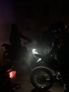 two motorcyclists in the dark with their bikes lit up at night time