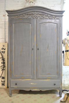 an old gray armoire with peeling paint on the doors and bottom part, next to a pair of shoes