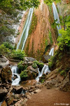 a waterfall in the middle of a forest with lots of rocks and trees around it