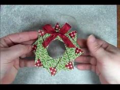 two hands are holding a green and red ornament with a bow on it