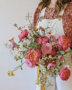 a woman in an apron holding a bouquet of flowers with pink and white blooms on it