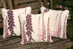 two pillows sitting on top of a wooden bench next to purple and white flowers with green leaves