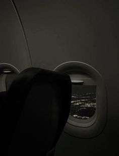 an airplane seat with the window open looking out at the city lights in the distance