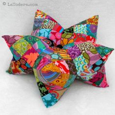 a multicolored star shaped pillow sitting on top of a white bed spreader