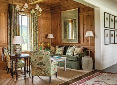 a living room with wood paneling and green couches, chairs, tables and lamps