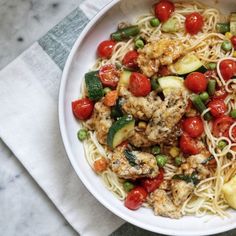 a white plate topped with pasta and veggies on top of a marble table