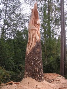 a carved wood sculpture of a woman on a tree stump in the woods with trees behind it