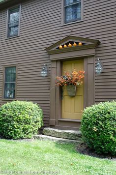 a brown house with a yellow door and some flowers on the window sill in front of it