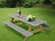 a picnic table in the middle of a grassy area with bottles of wine and fruit on it