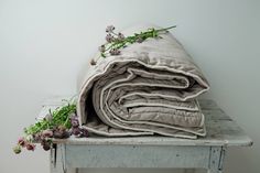 a stack of blankets sitting on top of a wooden table next to flowers and plants