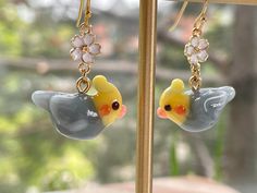 a pair of yellow and gray bird earrings hanging from gold - tone earwires