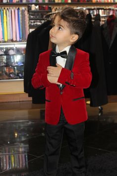 a young boy dressed in a red velvet suit and bow tie with his hands on his chest