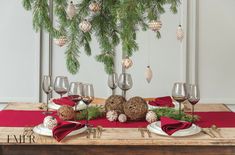 a wooden table topped with wine glasses and christmas decorations next to a pine branch filled with ornaments