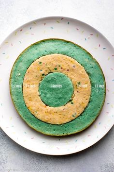 a green and yellow doughnut on a white plate with sprinkles around it