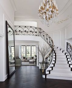 an elegant staircase with chandelier and mirror in the center is flanked by black wood flooring