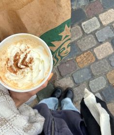 a person holding up a cup of coffee with whipped cream on top in their hand