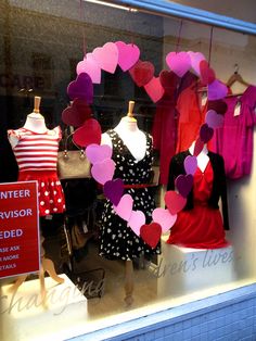 heart shaped paper hearts are hanging in the window of a clothing store on valentine's day