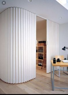 a room with a desk, chair and large white curtained partition in the wall