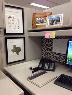 a desk with a computer, phone and pictures on the wall above it in an office cubicle