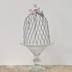 a glass cake stand with a bird on top and a pink bow around the top