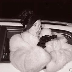 a woman in a fur coat leaning out the window of a car with her hand on her shoulder