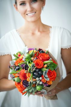 a woman in white holding a bouquet of orange flowers and greenery on her wedding day