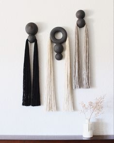 three black and white tassels hanging on the wall next to a vase with flowers