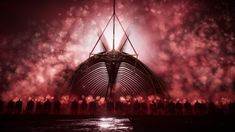 fireworks are lit up in the night sky over a large structure with people standing around it