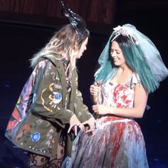 two women dressed in costumes standing next to each other with blue hair and horns on their heads