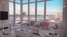 a living room filled with white furniture and large windows overlooking the cityscape in the distance