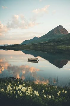 a small boat floating on top of a lake next to a lush green hillside covered in flowers