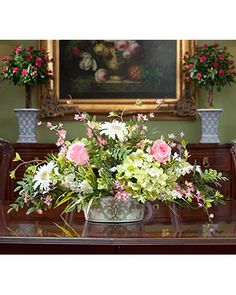 a vase filled with flowers sitting on top of a wooden table next to a painting