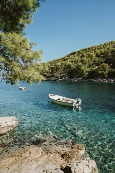 a boat floating on top of a body of water next to a rocky shore covered in green trees