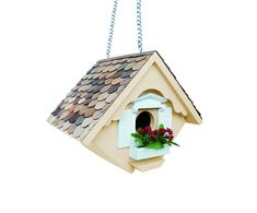 a bird house hanging from a chain with flowers in the window and on it's side