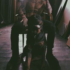 a man sitting in a chair next to a dog with tattoos on his arm and chest