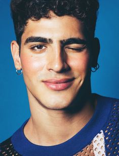 a close up of a person with curly hair and piercings on his ears, wearing a blue sweater