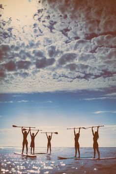 four people are standing on surfboards in the water with their arms raised above their heads