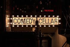 a sign that says comedy cellar lit up at night with lights on the side of it