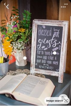 an open book sitting on top of a table next to a vase with flowers and a chalkboard sign