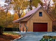 a garage with a red door in front of some trees and leaves on the ground