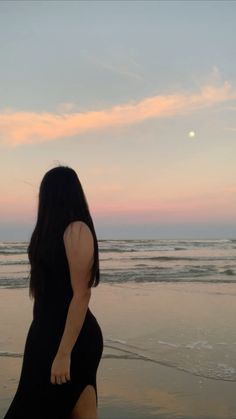 a woman walking on the beach at sunset